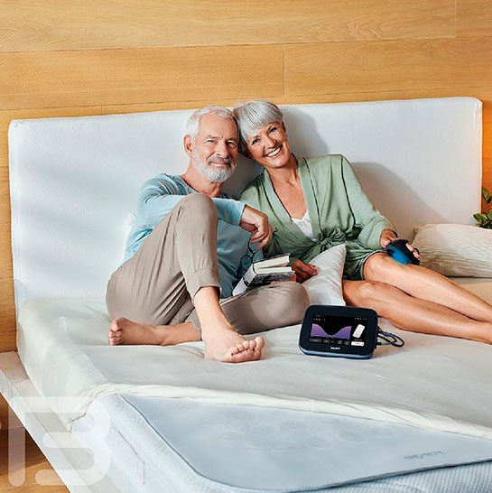 Una parella sotmesa al tractament de Teràpia BEMER mentre està asseguda en un llit amb coixinet tèrmic.