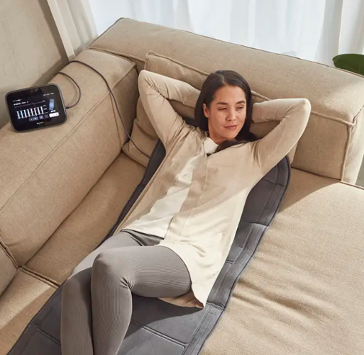Una dona estirada en un sofà amb un coixinet elèctric.
