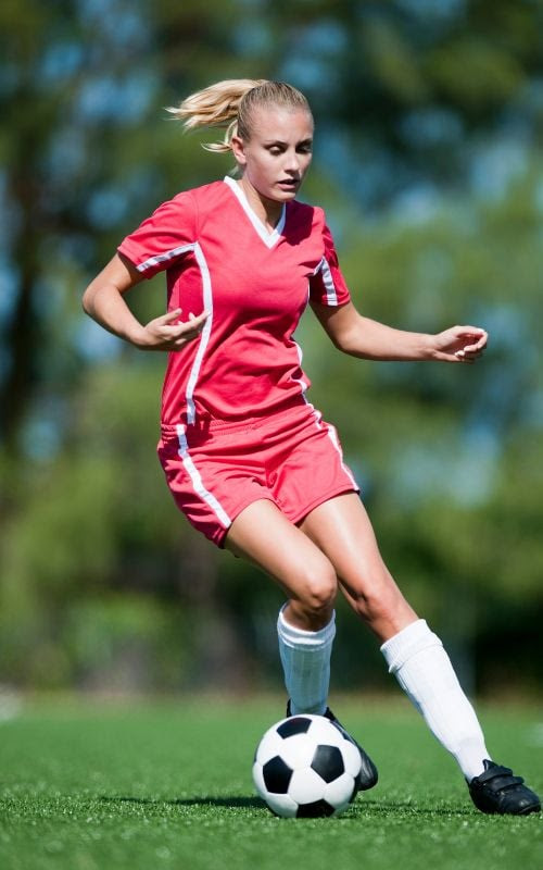 Una noia amb un uniforme de futbol vermell donant cops a una pilota.